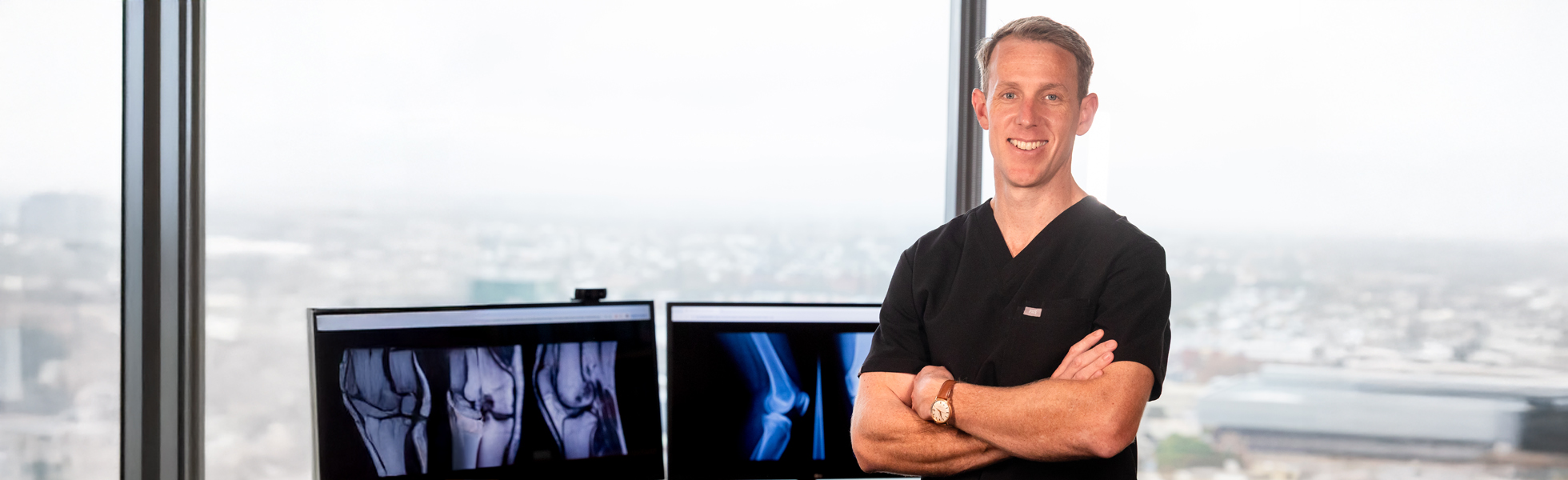 Orthopaedic surgeon Dr. David standing confidently in front of knee X-rays in a high-rise medical office